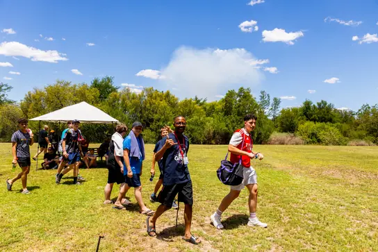 Campers walking across a sunny field past a gazebo