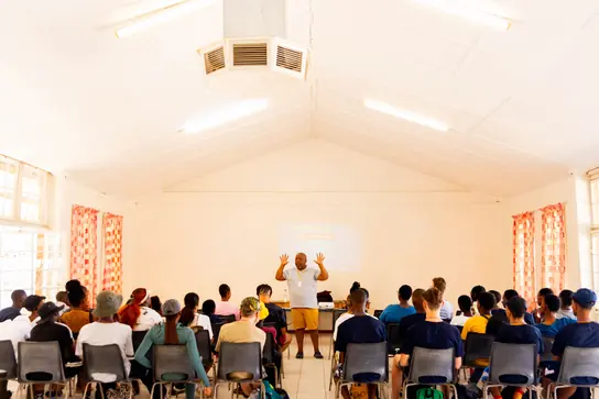 A leader speaking to seated campers in a bright hall
