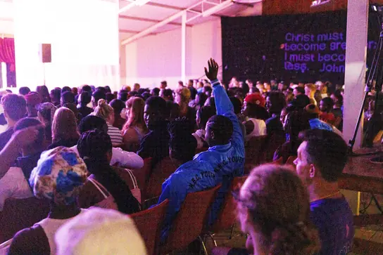 Campers with raised hands in a dark, crowded hall